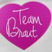 Pinkfarbenes Stoff-Herz mit Team Braut-Stick auf grauem Beutel